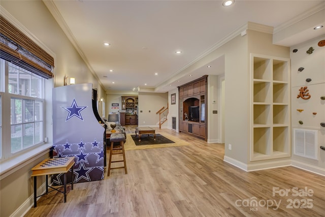 living room featuring built in shelves, light wood-type flooring, and crown molding