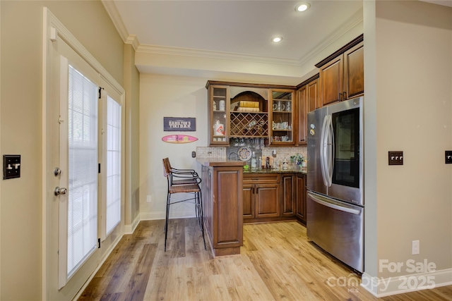 bar featuring ornamental molding, backsplash, stainless steel refrigerator, and light hardwood / wood-style flooring