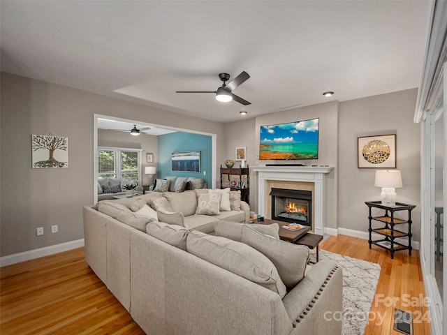 living room with ceiling fan, light wood-type flooring, and a fireplace