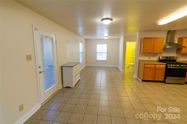 kitchen with stainless steel gas range oven, wall chimney range hood, a textured ceiling, and light tile patterned floors