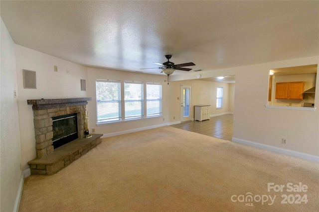 unfurnished living room featuring ceiling fan, a stone fireplace, plenty of natural light, and carpet floors