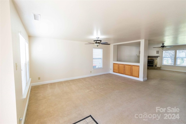 unfurnished living room featuring ceiling fan, light colored carpet, and a brick fireplace