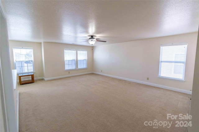 carpeted empty room with a textured ceiling, plenty of natural light, and ceiling fan