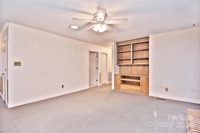 unfurnished living room with ceiling fan, built in features, light colored carpet, and a textured ceiling