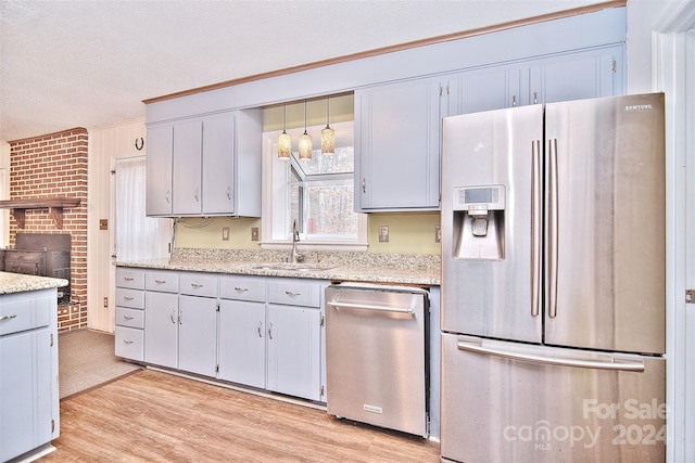 kitchen featuring pendant lighting, sink, a textured ceiling, appliances with stainless steel finishes, and brick wall