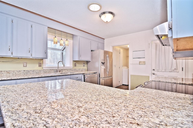 kitchen featuring sink, light stone countertops, a textured ceiling, appliances with stainless steel finishes, and washer / clothes dryer