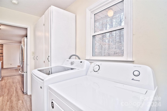 clothes washing area featuring light wood-type flooring, independent washer and dryer, and a textured ceiling