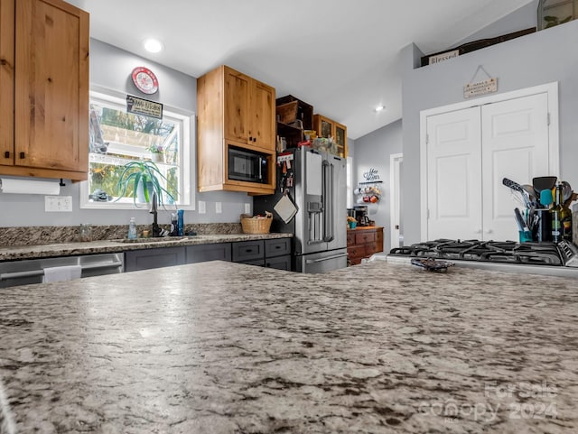 kitchen featuring light stone counters, sink, lofted ceiling, and appliances with stainless steel finishes