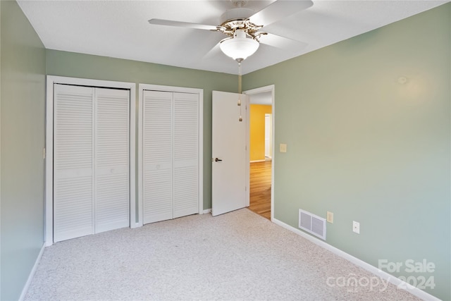 unfurnished bedroom featuring carpet flooring, ceiling fan, and two closets