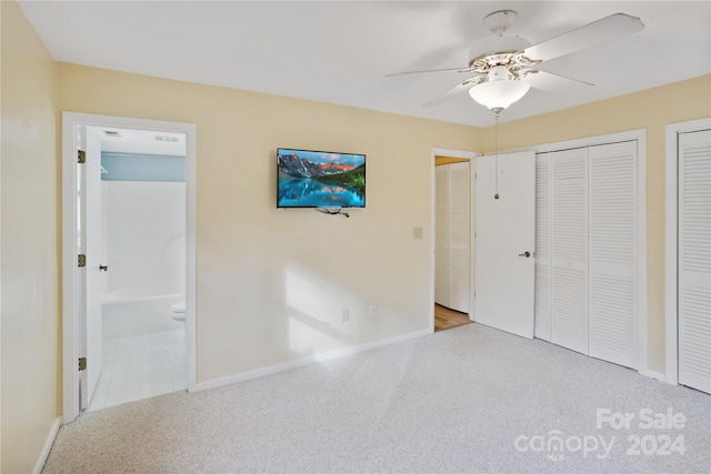 unfurnished bedroom with connected bathroom, ceiling fan, light colored carpet, and multiple closets