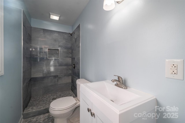 bathroom with toilet, vanity, and a tile shower