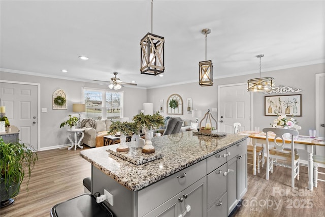 kitchen featuring crown molding, hanging light fixtures, light hardwood / wood-style flooring, a kitchen island, and light stone countertops