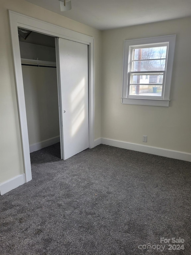 unfurnished bedroom with dark carpet and a closet