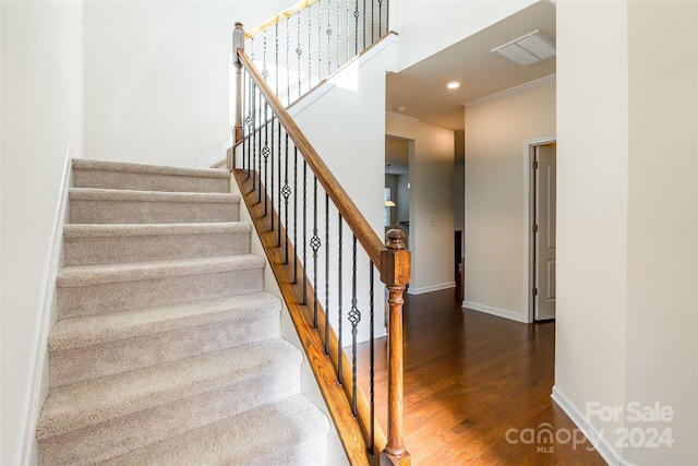 stairs with wood-type flooring and crown molding