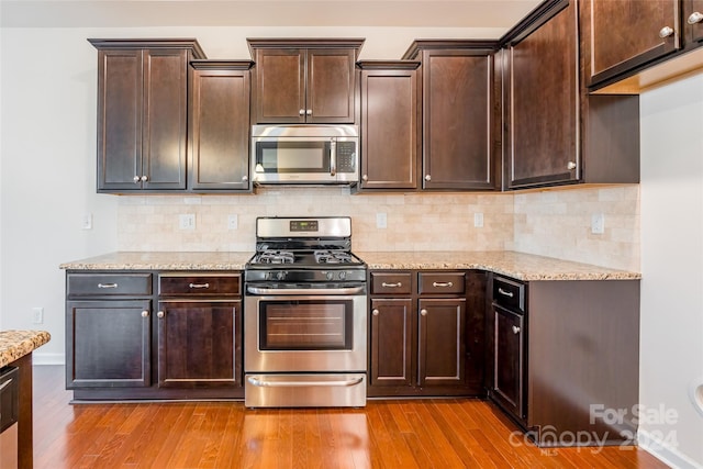 kitchen with dark brown cabinets, light hardwood / wood-style floors, light stone countertops, and appliances with stainless steel finishes