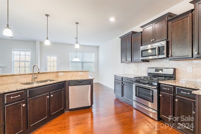 kitchen featuring dark brown cabinetry, sink, backsplash, pendant lighting, and appliances with stainless steel finishes