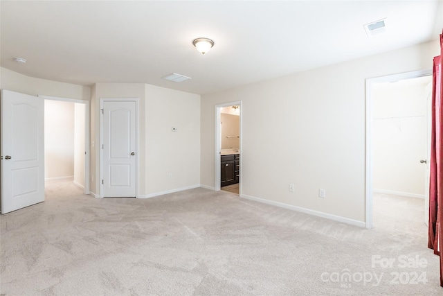 unfurnished bedroom featuring a spacious closet, light carpet, connected bathroom, and a closet