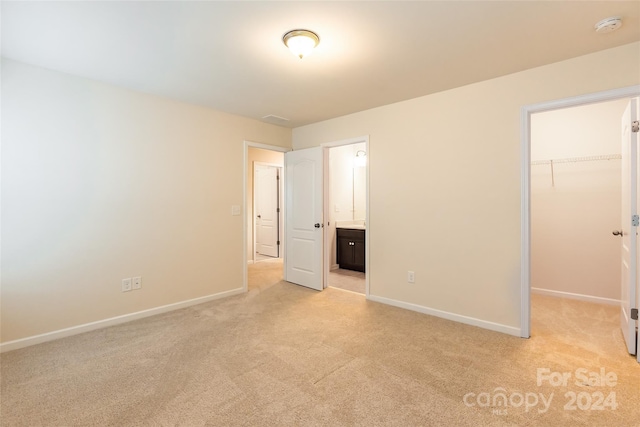 unfurnished bedroom with ensuite bath, a spacious closet, a closet, and light carpet