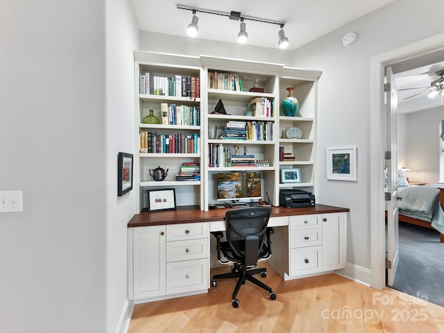 home office featuring ceiling fan, built in desk, and light hardwood / wood-style flooring