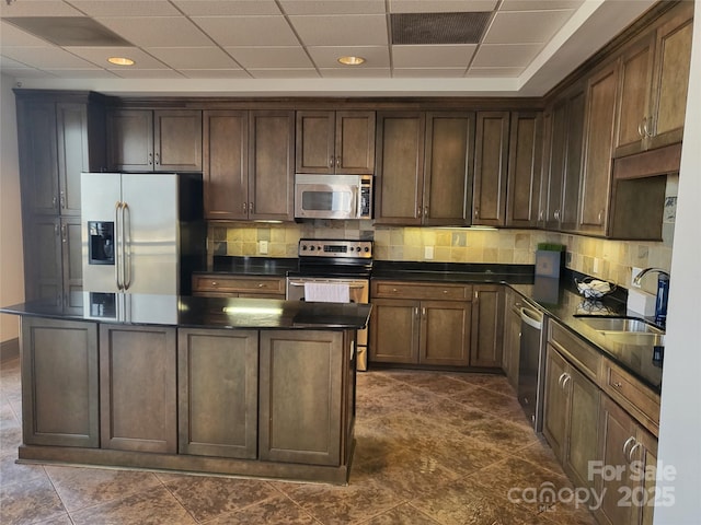 kitchen with dark brown cabinetry, sink, a center island, decorative backsplash, and appliances with stainless steel finishes