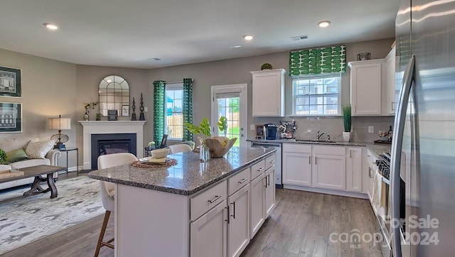 kitchen with light wood-type flooring, appliances with stainless steel finishes, a kitchen island, light stone counters, and white cabinetry