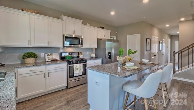 kitchen with light stone countertops, appliances with stainless steel finishes, tasteful backsplash, white cabinets, and light hardwood / wood-style floors