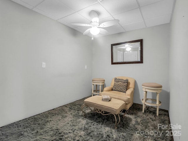 living area with ceiling fan, a drop ceiling, and carpet