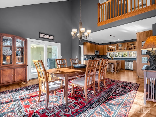 dining area with light hardwood / wood-style flooring, a high ceiling, and an inviting chandelier