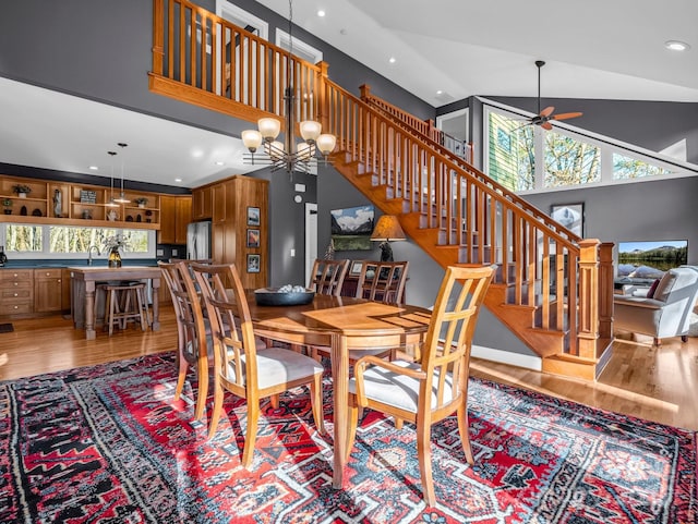 dining area with ceiling fan with notable chandelier, light wood-type flooring, sink, and a towering ceiling