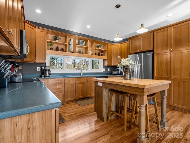 kitchen featuring appliances with stainless steel finishes, light wood-type flooring, a kitchen breakfast bar, sink, and pendant lighting