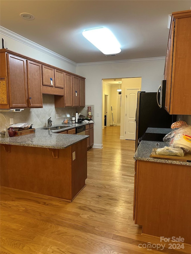 kitchen featuring sink, ornamental molding, kitchen peninsula, a breakfast bar, and light wood-type flooring