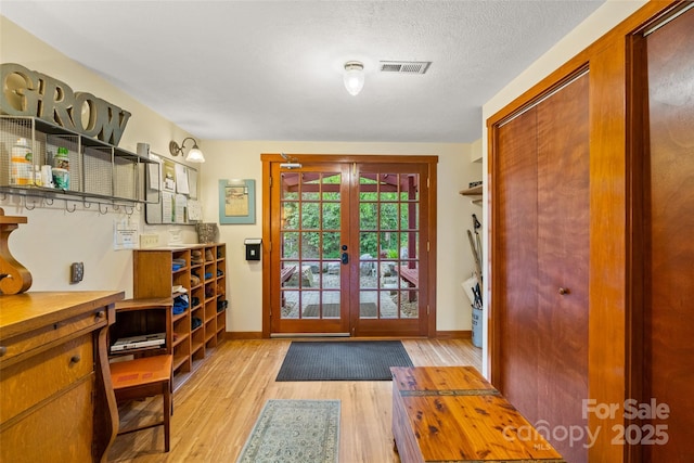 doorway with a textured ceiling, light hardwood / wood-style flooring, and french doors