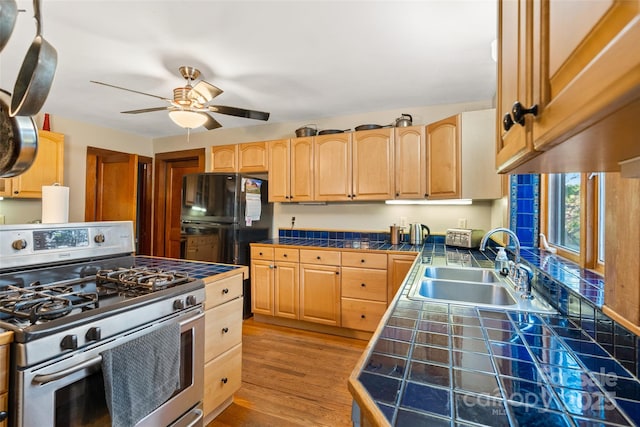 kitchen featuring tile countertops, sink, stainless steel range with gas stovetop, light hardwood / wood-style flooring, and light brown cabinetry