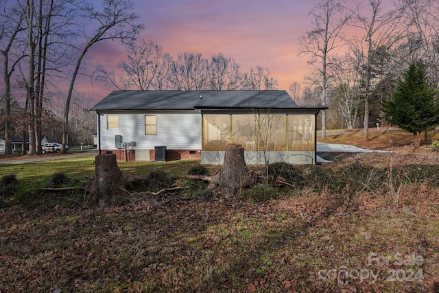 back house at dusk featuring a sunroom and central air condition unit