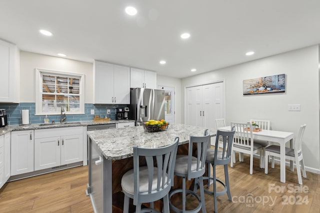 kitchen featuring white cabinetry, light stone countertops, sink, stainless steel refrigerator with ice dispenser, and a kitchen island