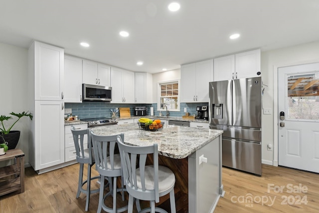 kitchen featuring light stone counters, stainless steel appliances, white cabinets, a center island, and a breakfast bar area