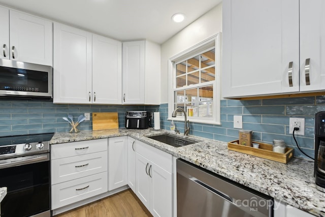 kitchen with tasteful backsplash, sink, white cabinets, and stainless steel appliances