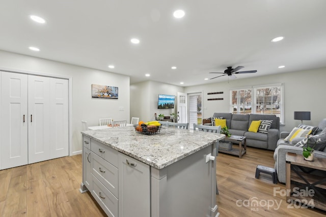 kitchen featuring ceiling fan, light stone counters, light hardwood / wood-style flooring, a breakfast bar area, and a kitchen island