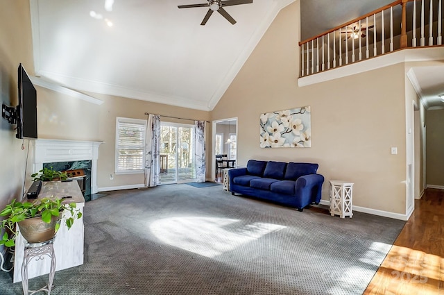 living room with ceiling fan, crown molding, dark colored carpet, high vaulted ceiling, and a fireplace