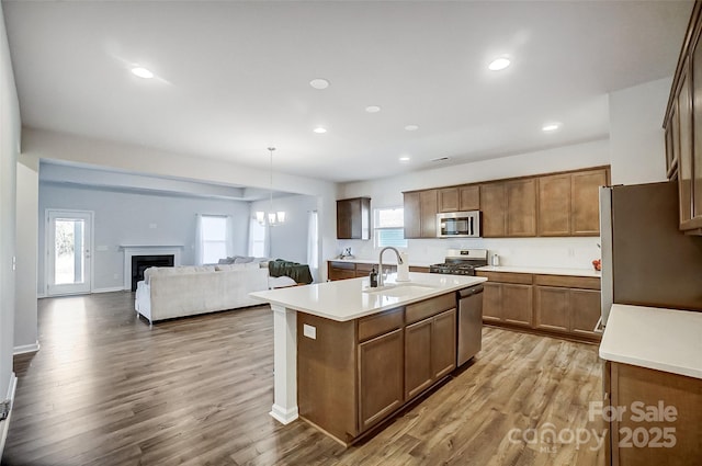 kitchen with sink, an island with sink, decorative light fixtures, light hardwood / wood-style floors, and stainless steel appliances