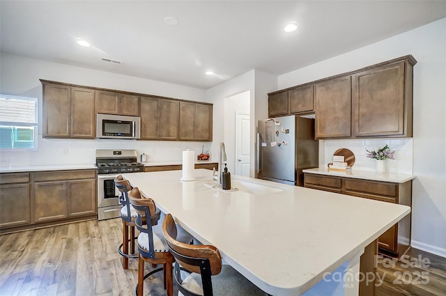 kitchen with sink, stainless steel appliances, a breakfast bar area, a center island with sink, and light wood-type flooring