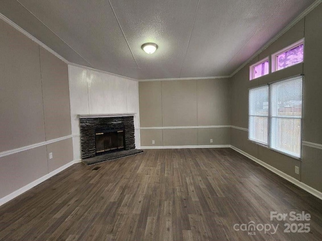 unfurnished living room with a stone fireplace, a textured ceiling, crown molding, and dark wood finished floors