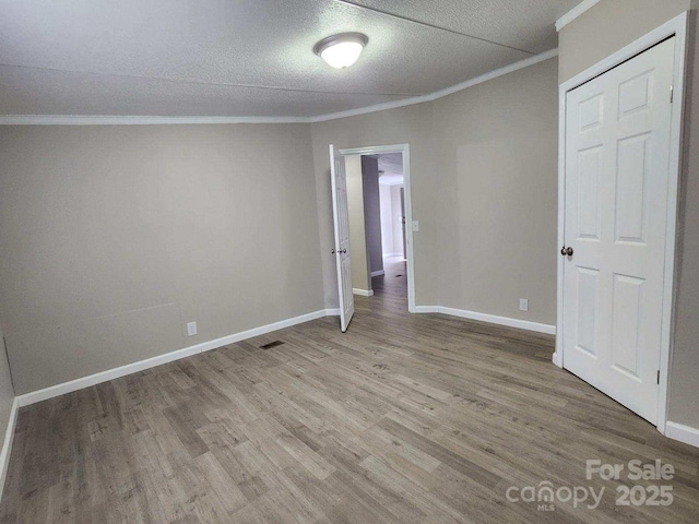 interior space featuring baseboards, ornamental molding, a textured ceiling, visible vents, and wood finished floors