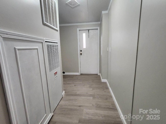 corridor featuring light wood-style flooring, baseboards, ornamental molding, and visible vents