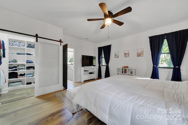 bedroom featuring hardwood / wood-style flooring, ceiling fan, and a barn door