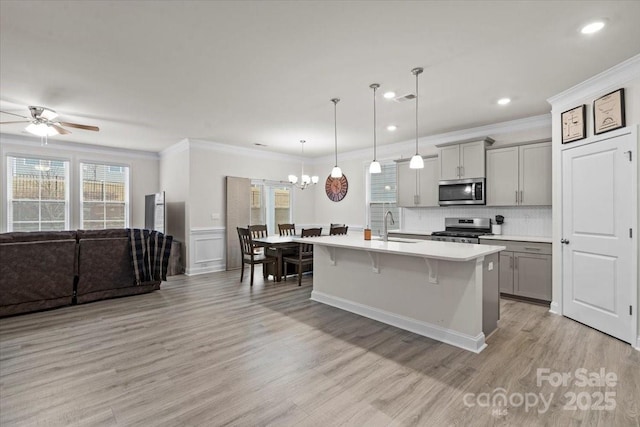 kitchen with gray cabinetry, a kitchen island with sink, hanging light fixtures, sink, and appliances with stainless steel finishes