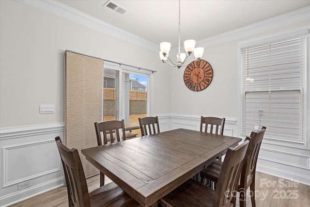 dining space with ornamental molding, light wood-type flooring, and a notable chandelier