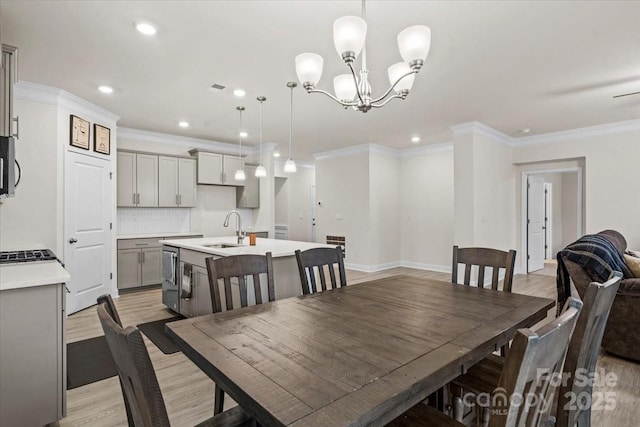 dining area featuring ornamental molding, light wood-type flooring, sink, and a chandelier