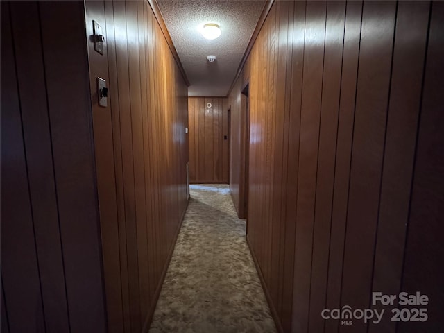 corridor with light carpet, a textured ceiling, and wood walls