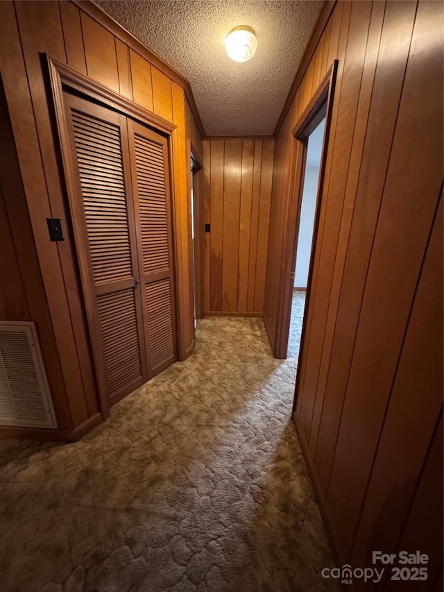 corridor with carpet floors, a textured ceiling, and wooden walls